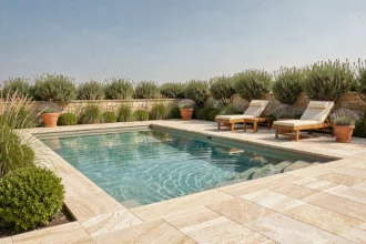 Aménagement des abords d'une piscine avec carrelage en travertin, transats en teck et plantes méditerranéennes